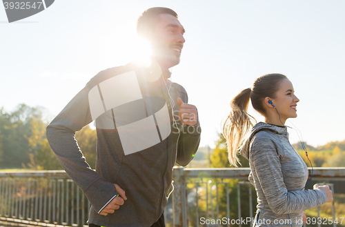 Image of happy couple with earphones running outdoors