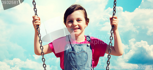 Image of happy little girl swinging on swing over blue sky