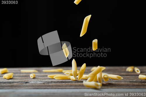 Image of Falling penne pasta. Flying yellow raw macaroni over black background.