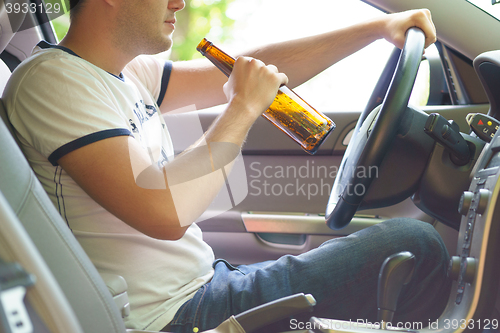 Image of Man drinking beer while driving the car.