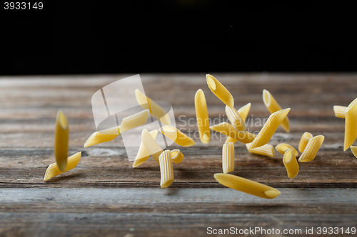 Image of Falling penne pasta. Flying yellow raw macaroni over black background.
