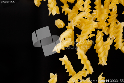 Image of Falling fusilli pasta. Flying yellow raw macaroni over black background.