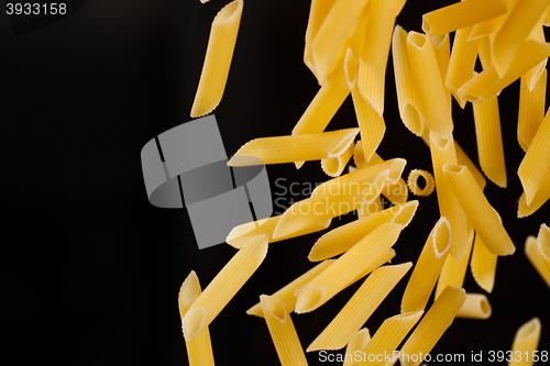Image of Falling penne pasta. Flying yellow raw macaroni over black background.