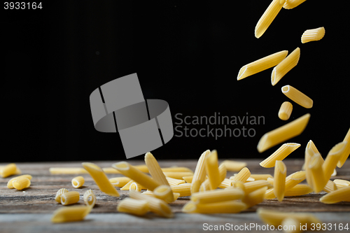 Image of Falling penne pasta. Flying yellow raw macaroni over black background.