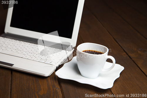 Image of Fresh black coffee in cup on saucer near laptop