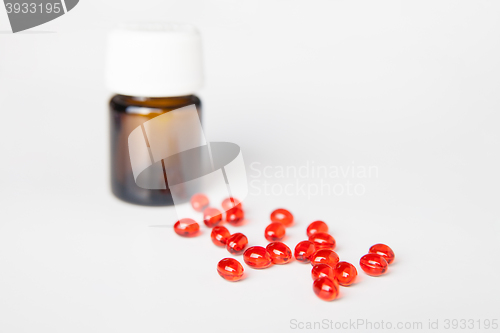 Image of Pile of red pills on white table. Bottle