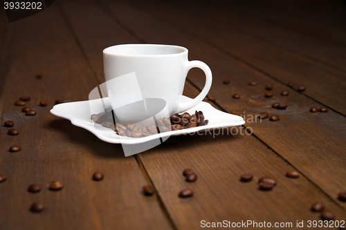 Image of Aromatic coffee in white cup with saucer and scattered beans