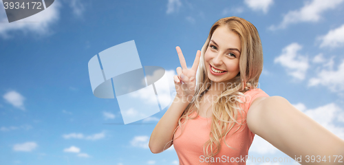 Image of smiling woman taking selfie and showing peace sign