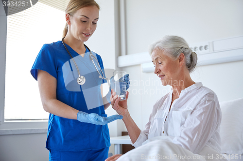 Image of nurse giving medicine to senior woman at hospital