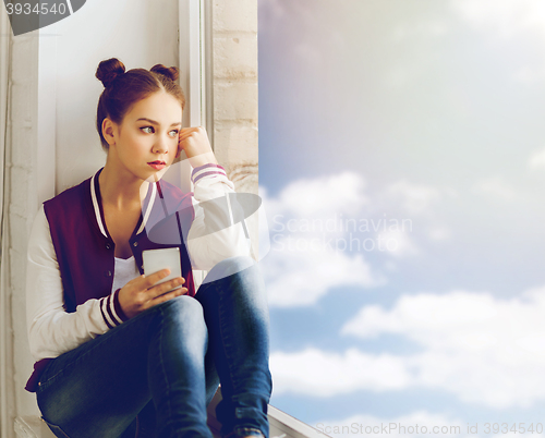 Image of teenage girl sitting on windowsill with smartphone