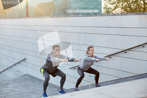 Image of couple doing squats on city street stairs