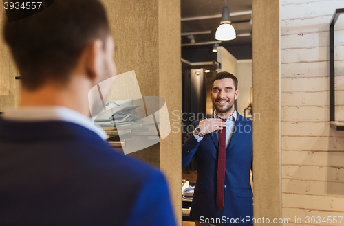 Image of man trying tie on at mirror in clothing store