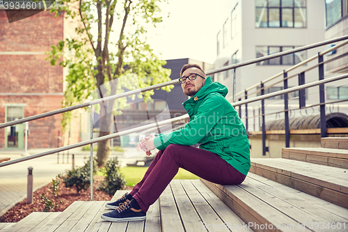 Image of happy young hipster man sitting on stairs in city