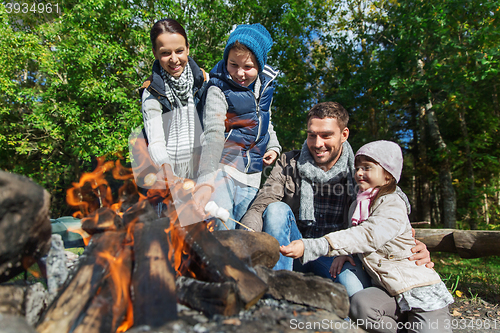 Image of happy family roasting marshmallow over campfire