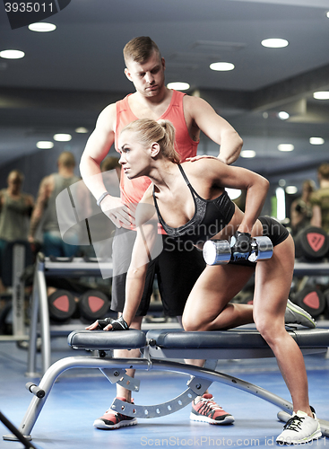 Image of young couple with dumbbell flexing muscles in gym
