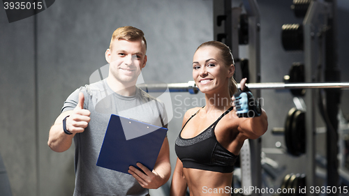 Image of smiling young woman with personal trainer in gym