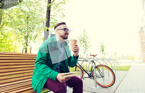 Image of happy hipster man eating sandwich with coffee