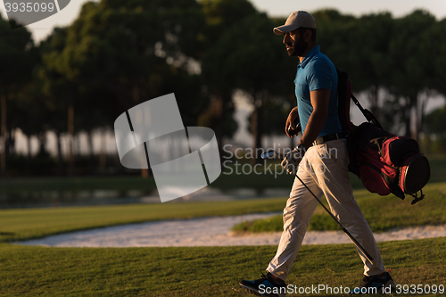 Image of golfer  walking and carrying golf  bag at beautiful sunset