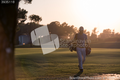 Image of golfer  walking and carrying golf  bag at beautiful sunset