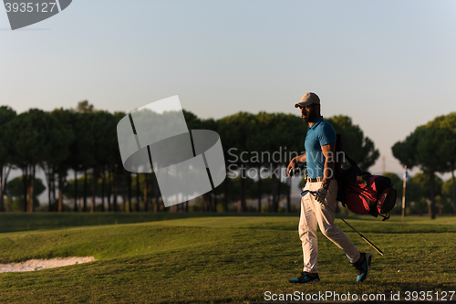 Image of golfer  walking and carrying golf  bag at beautiful sunset