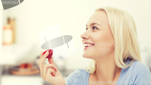 Image of happy woman eating strawberry on kitchen