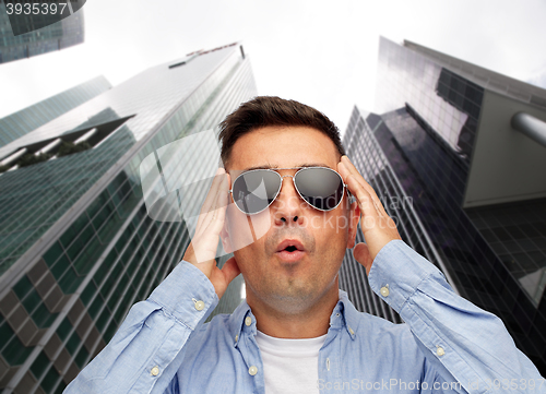 Image of face of scared man in sunglasses over big city