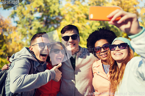 Image of smiling friends taking selfie with smartphone