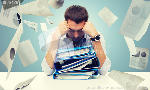 Image of sad businessman with stack of folders at office