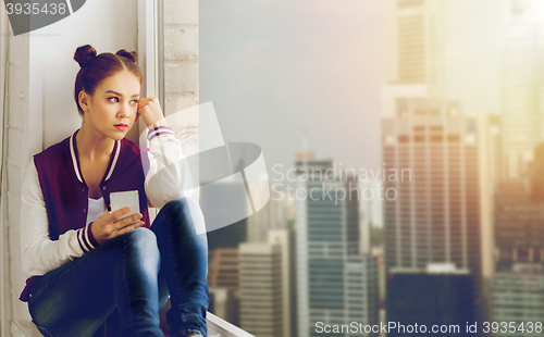 Image of teenage girl sitting on windowsill with smartphone