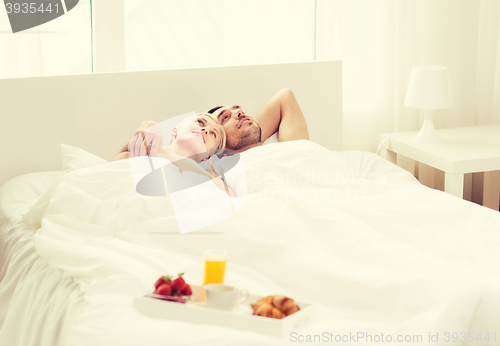 Image of happy couple lying in bed with tray of breakfast