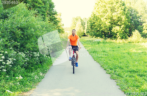 Image of happy young man riding bicycle outdoors