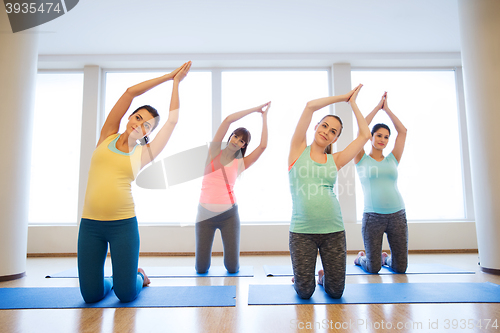 Image of happy pregnant women exercising on mats in gym