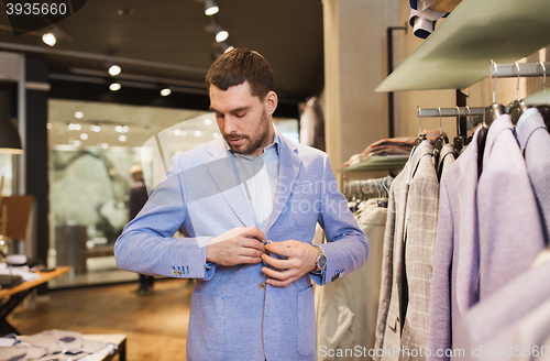 Image of happy young man trying jacket on in clothing store