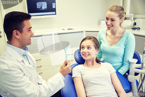 Image of happy dentist showing toothbrush to patient girl