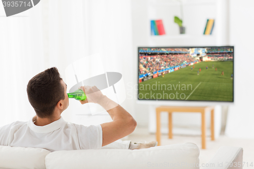 Image of man watching soccer game on tv and drinking beer