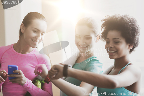 Image of happy women showing time on wrist watch in gym