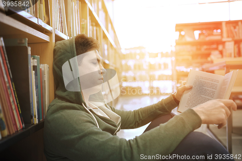 Image of student boy or young man reading book in library