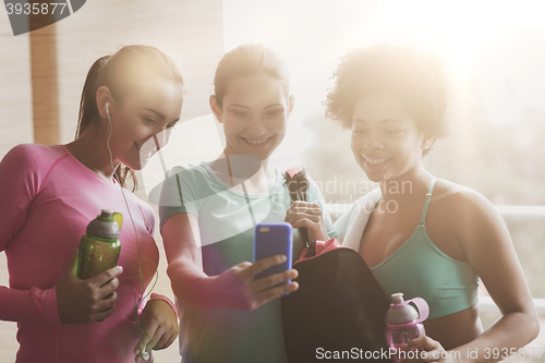 Image of happy women with bottles and smartphone in gym