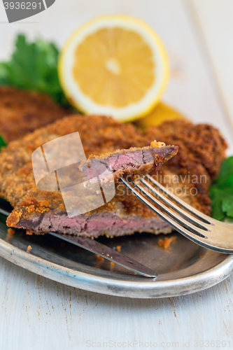 Image of Piece of beef schnitzel on a fork, lemon and parsley.