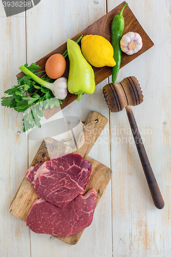 Image of Raw beef for schnitzel and vegetables on wooden plate. View from