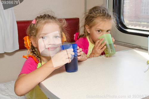 Image of Two little sisters in a train drinking tea at a table on the lower place in the second-class compartment wagon