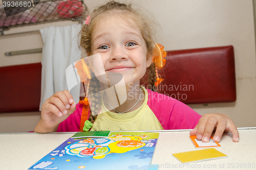 Image of Little girl on the train with a happy smile sitting at a table on the lower second-class place car and makes the applique