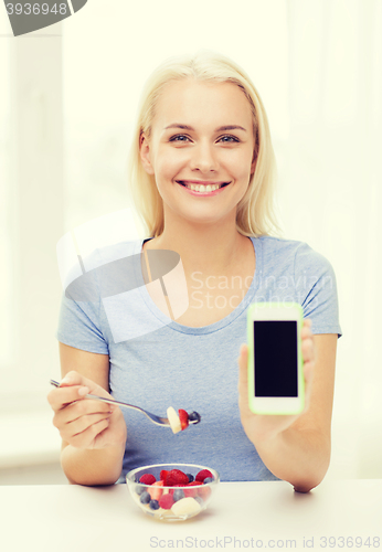 Image of woman with smartphone eating fruits at home
