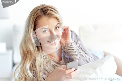 Image of happy young woman with smartphone in bed at home