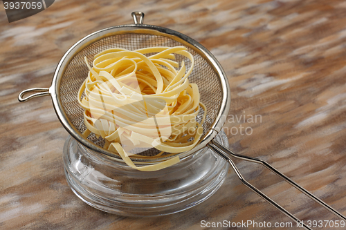 Image of Raw noodle pasta in metal kitchen sieve