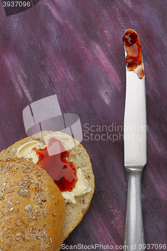 Image of Halved wholemeal roll with butter and red jam and knife with jam