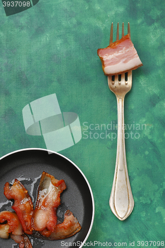 Image of Fried bacon on a pan and silver fork with raw bacon piece