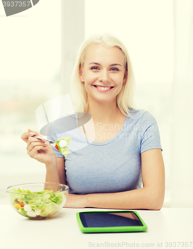 Image of smiling woman eating salad with tablet pc at home