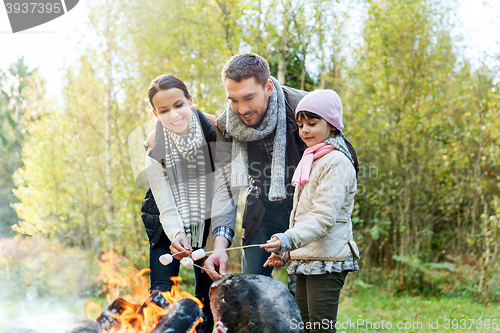 Image of happy family roasting marshmallow over campfire