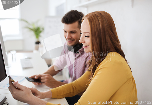 Image of happy creative team with smartphones at office